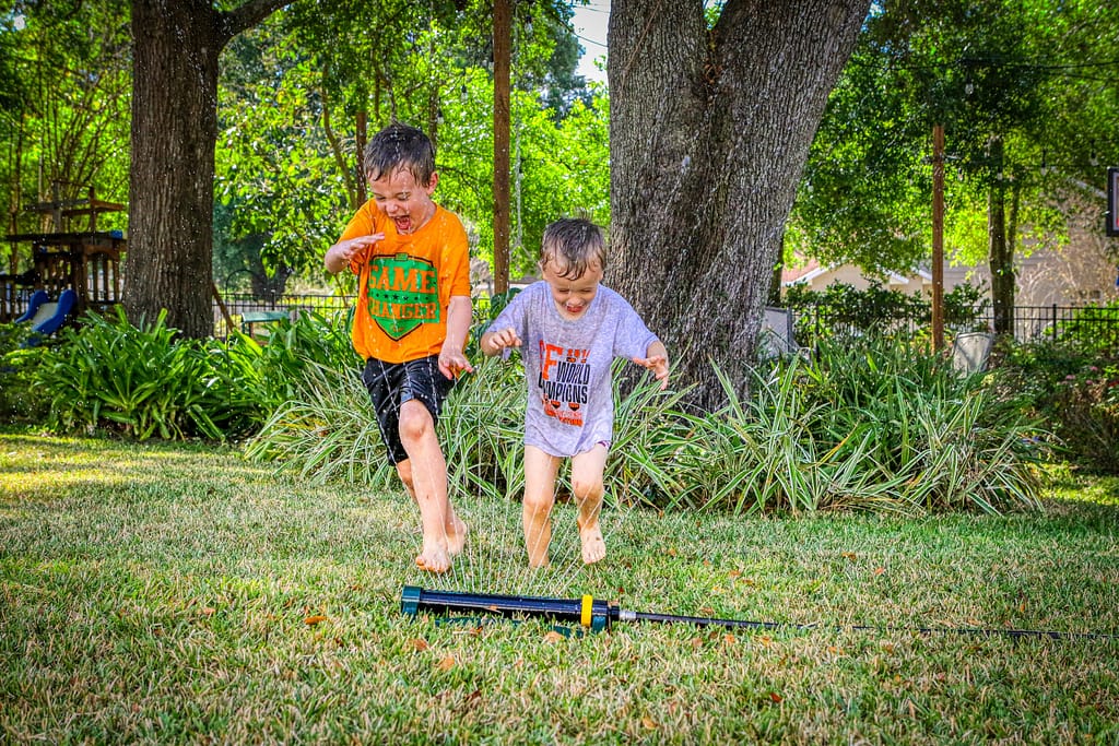 Brothers planing in the yard with sprinklers